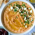 Spicy Feta Dip (Tirokafteri) in white bowl garnished with crumbled feta cheese and parsley surrounded by pita wedges.