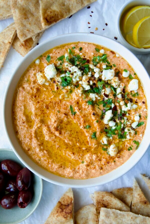 Spicy Feta Dip (Tirokafteri) in white bowl garnished with crumbled feta cheese and parsley surrounded by pita wedges.