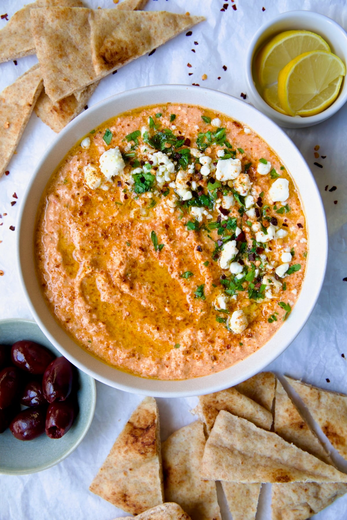 Spicy Feta Dip (Tirokafteri) in white bowl garnished with crumbled feta cheese and parsley surrounded by pita wedges.
