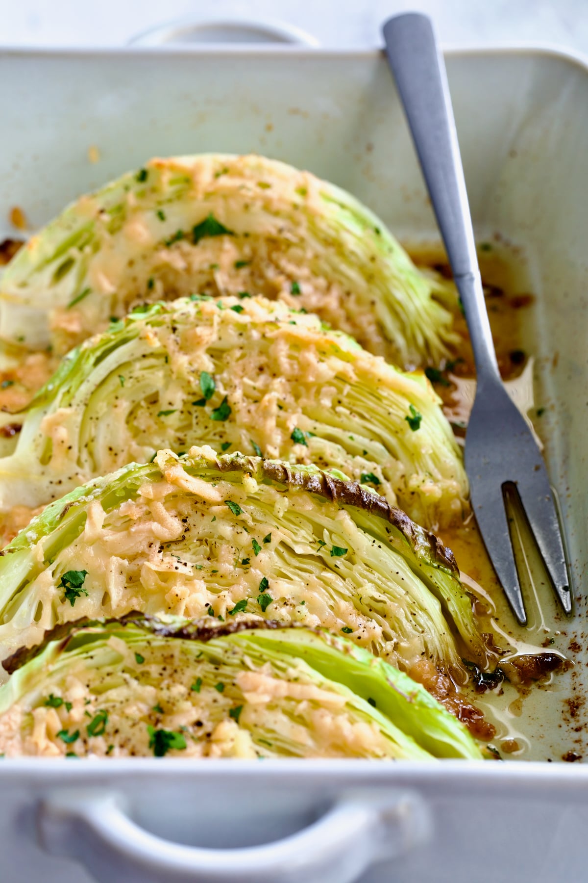Baked Garlic Parmesan Cabbage Wedges in white baking dish with serving fork.