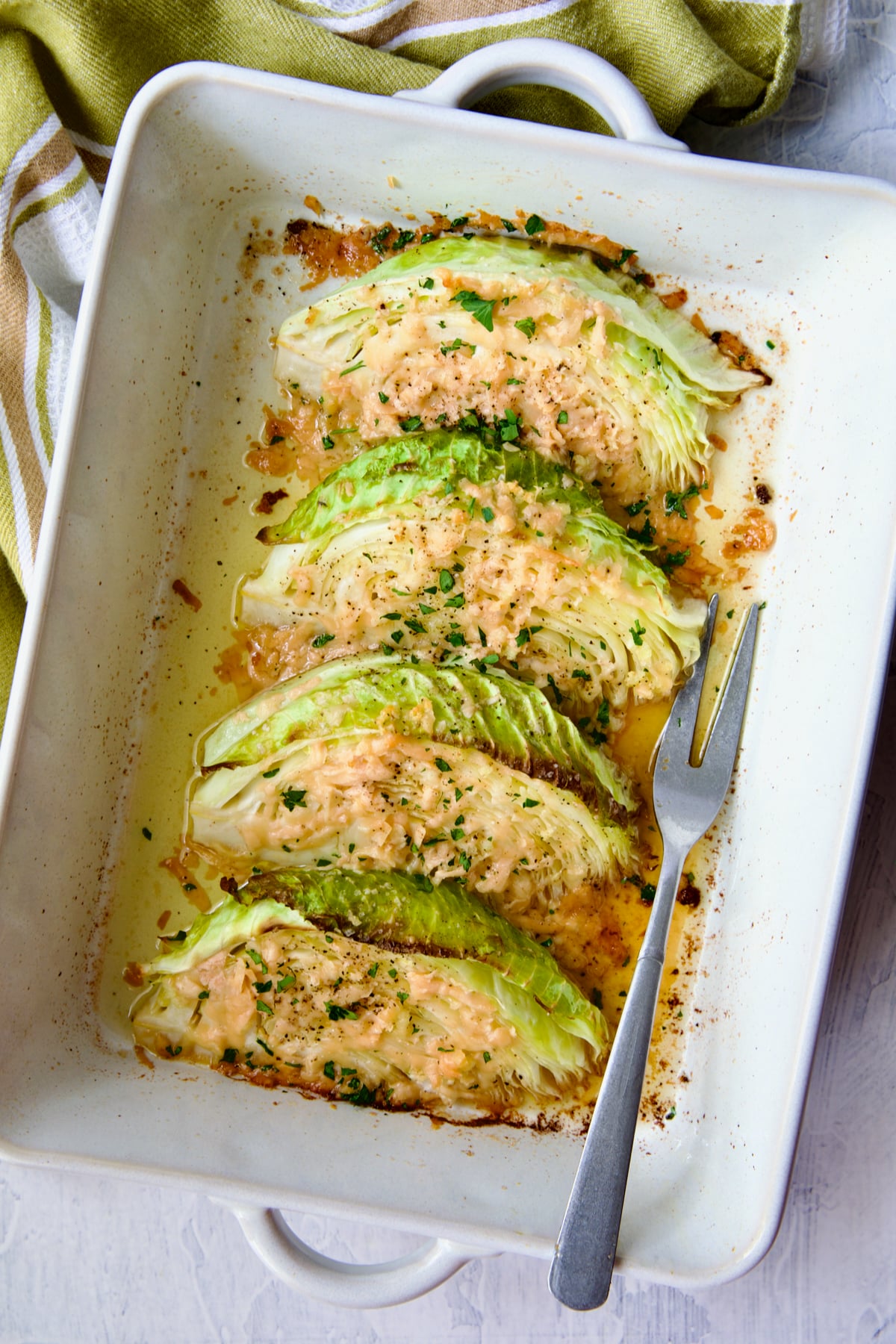 Baked Garlic Parmesan Cabbage Wedges in white baking dish with serving fork.