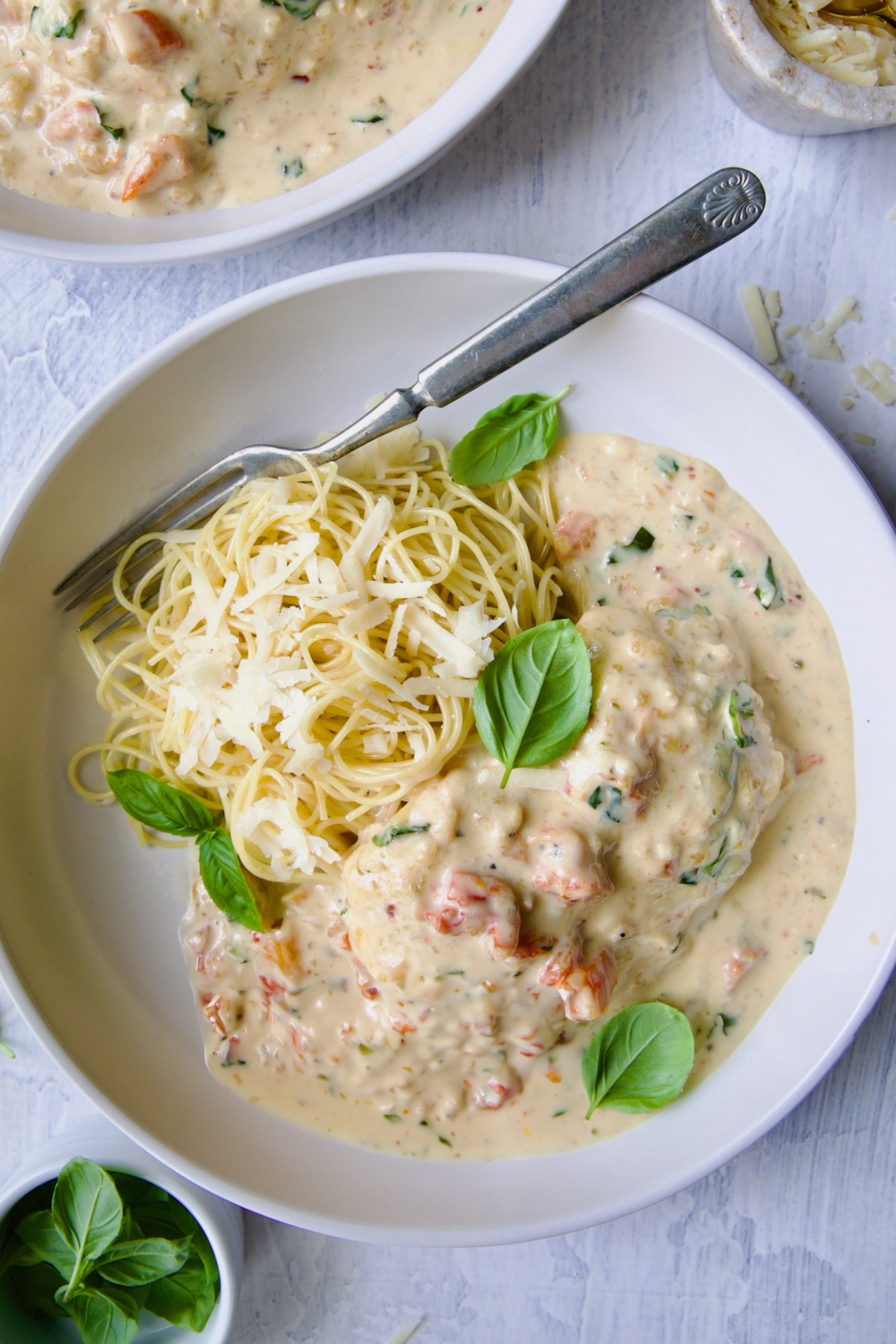 Marry Me Chicken in white bowl with angel hair pasta and fork garnished with fresh basil leaves.