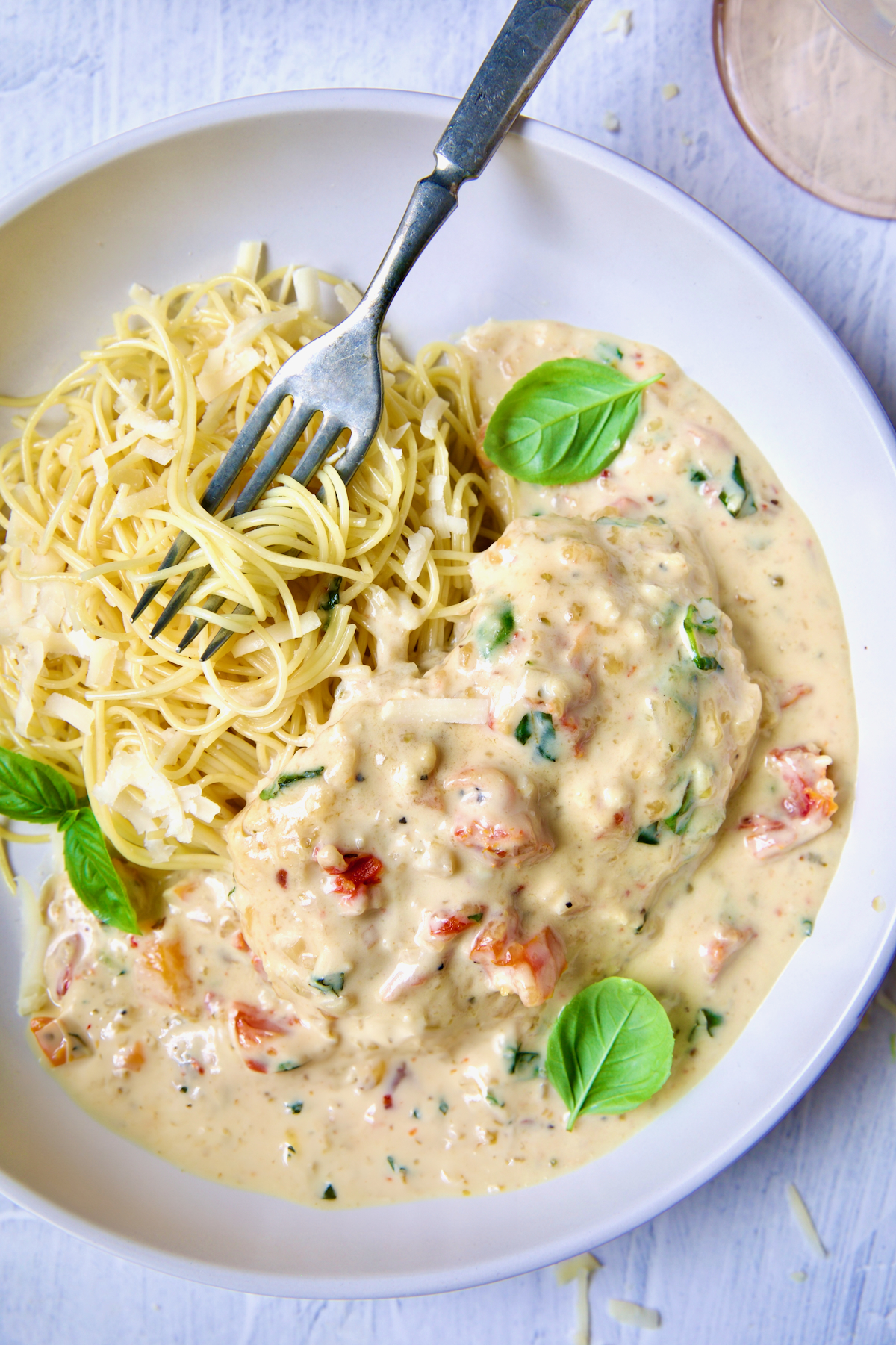 One serving of Marry Me Chicken in white bowl with angel hair pasta and fork garnished with fresh basil leaves.