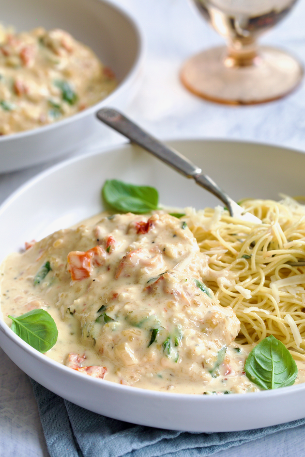 One serving of Marry Me Chicken in white bowl with angel hair pasta and fork garnished with fresh basil leaves.