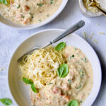 Marry Me Chicken in white bowl with angel hair pasta and fork garnished with fresh basil leaves.