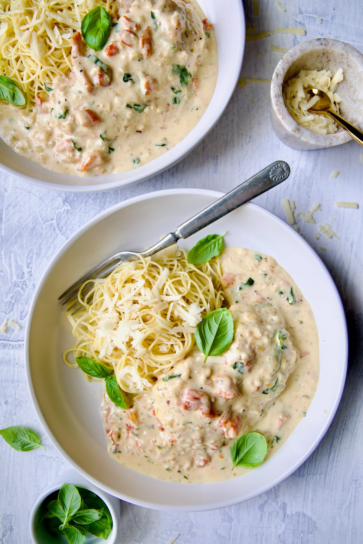 Marry Me Chicken in white bowl with angel hair pasta and fork garnished with fresh basil leaves.