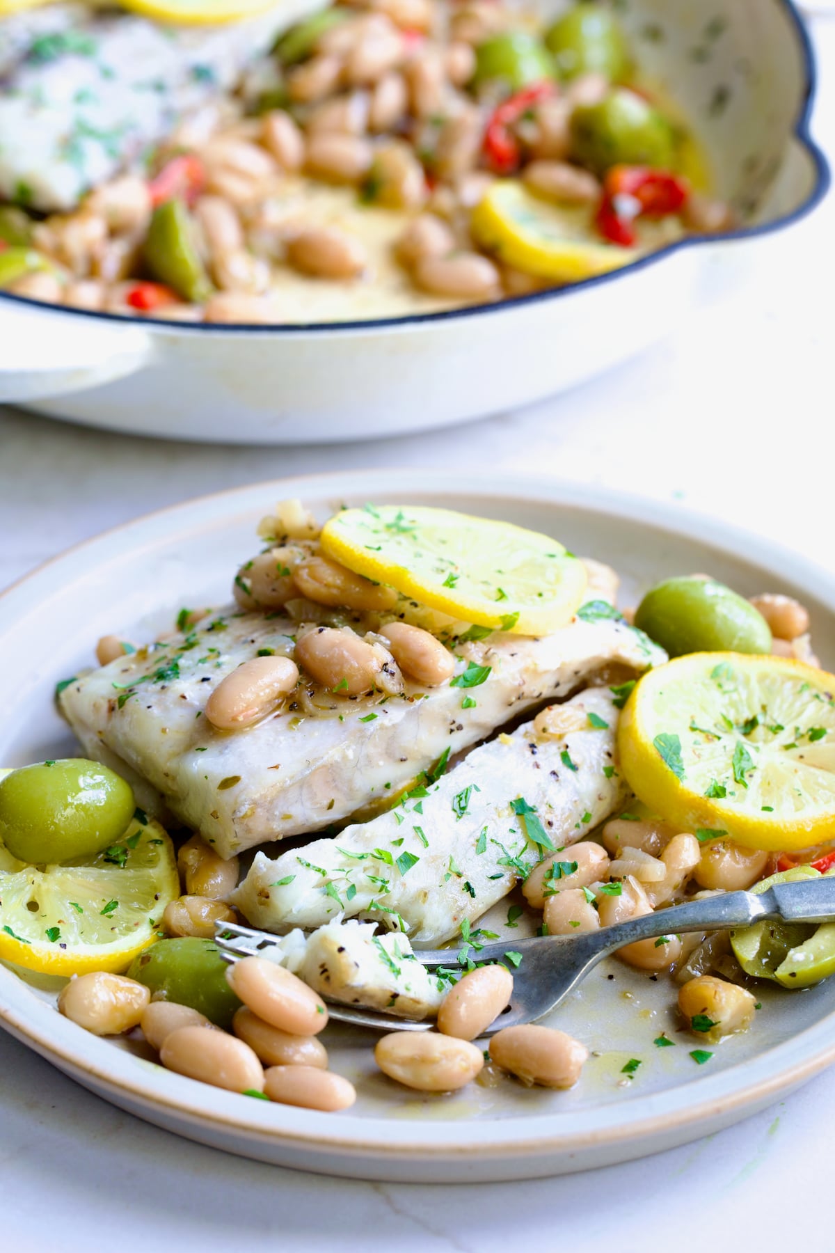 Serving of Mediterranean Fish and White Bean Skillet on round white plate.