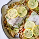 Mediterranean Fish and White Bean Skillet in white cast iron skillet topped with lemon slices.