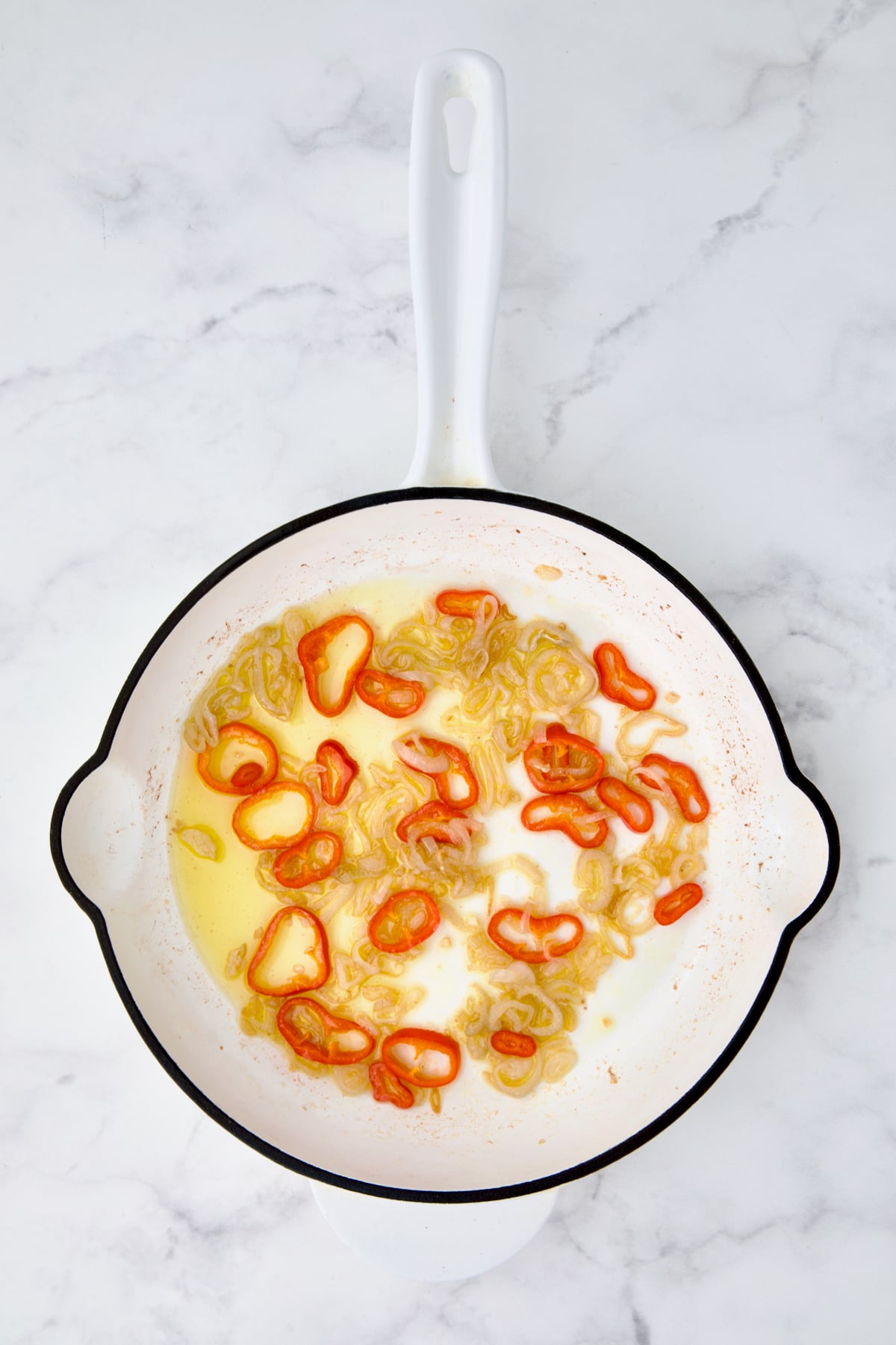 Sauteed shallot rings and Fresno chile in white cast iron skillet in olive oil.