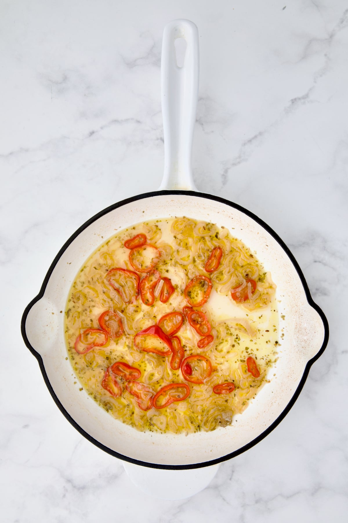 White wine and oregano added to sauteed shallot rings and Fresno chiles in white cast iron skillet.