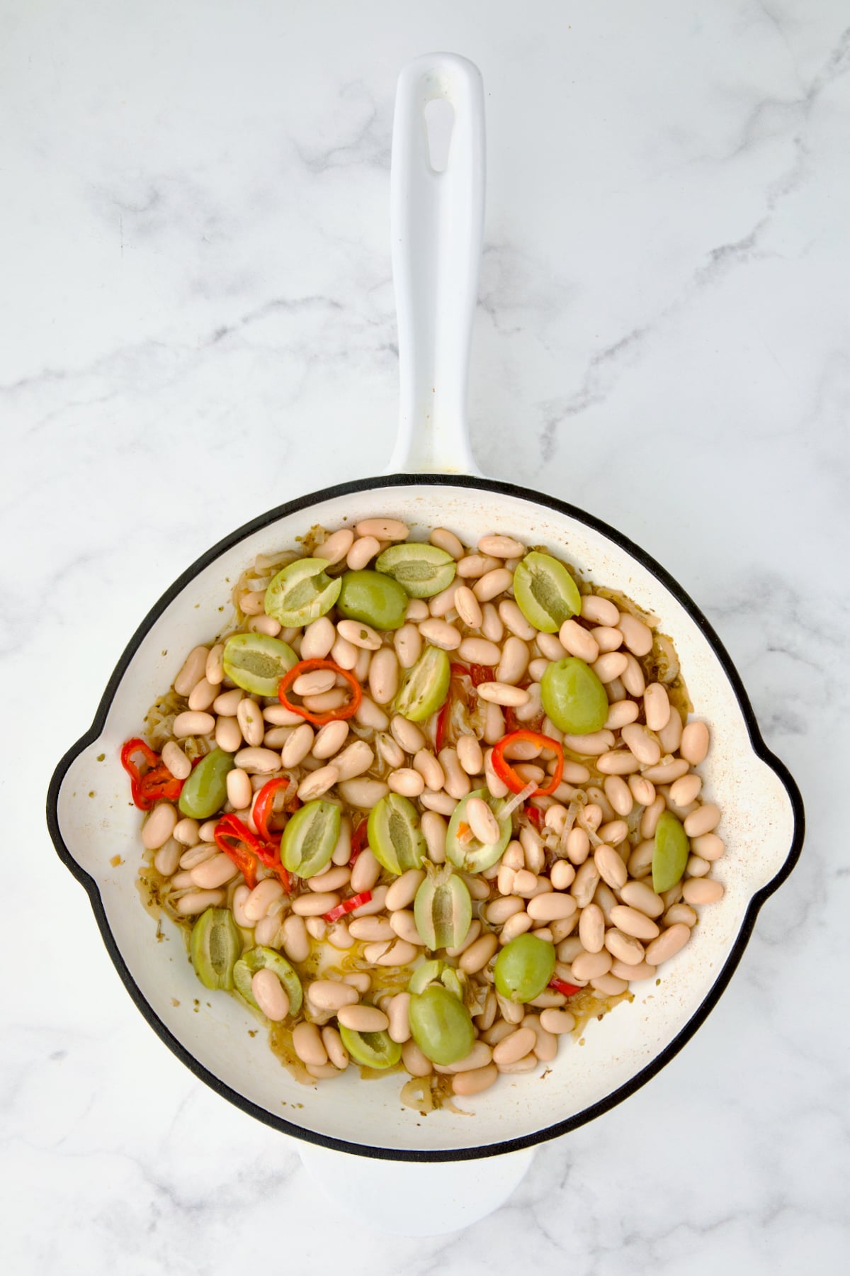 Beans and olives added to wine, oregano, shallot and Fresno chiles in white cast iron skillet.