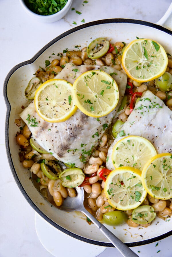 Mediterranean Fish and White Bean Skillet in white cast iron skillet topped with lemon slices.
