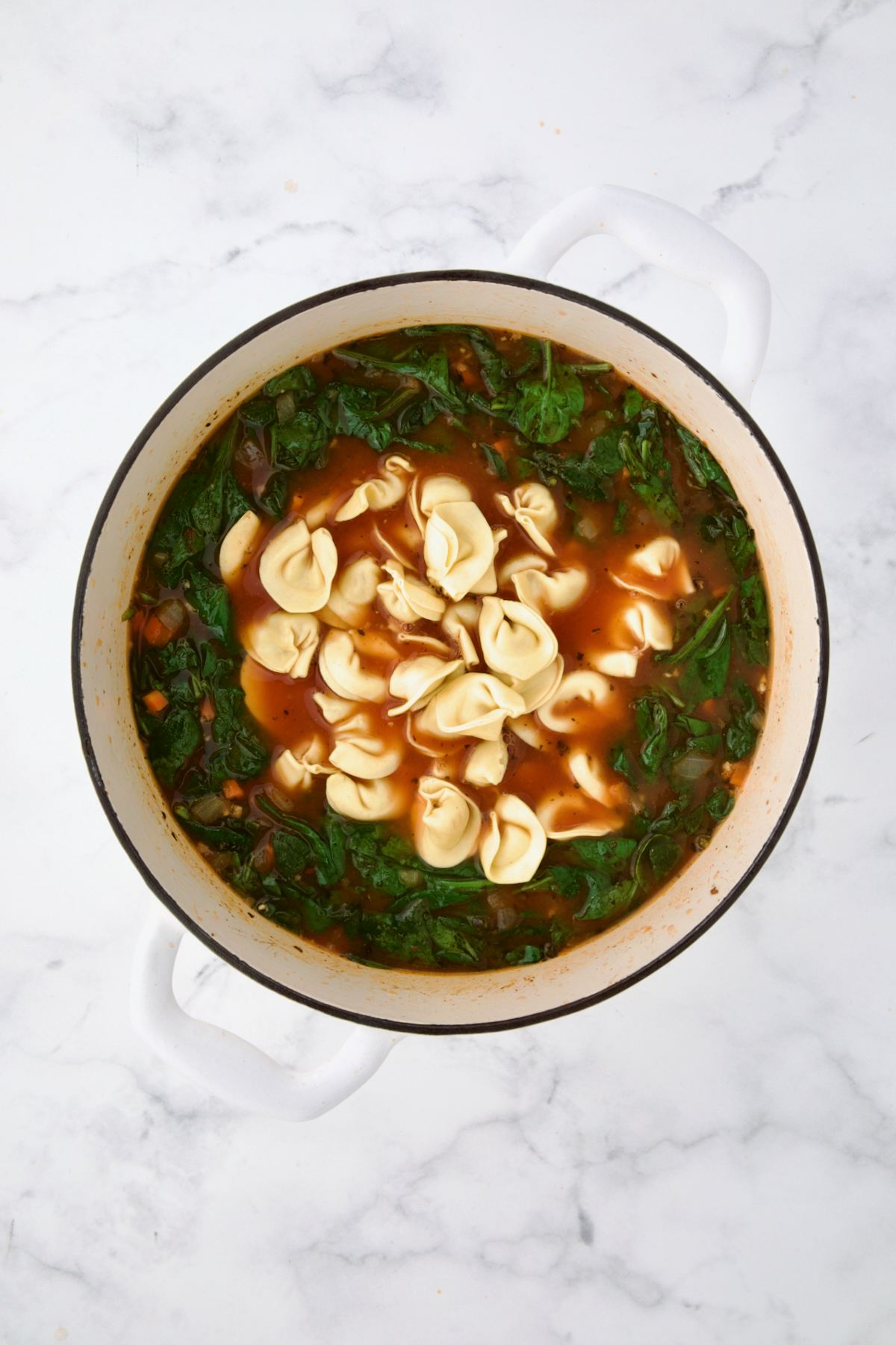 Tortellini added to soup in white Dutch oven.