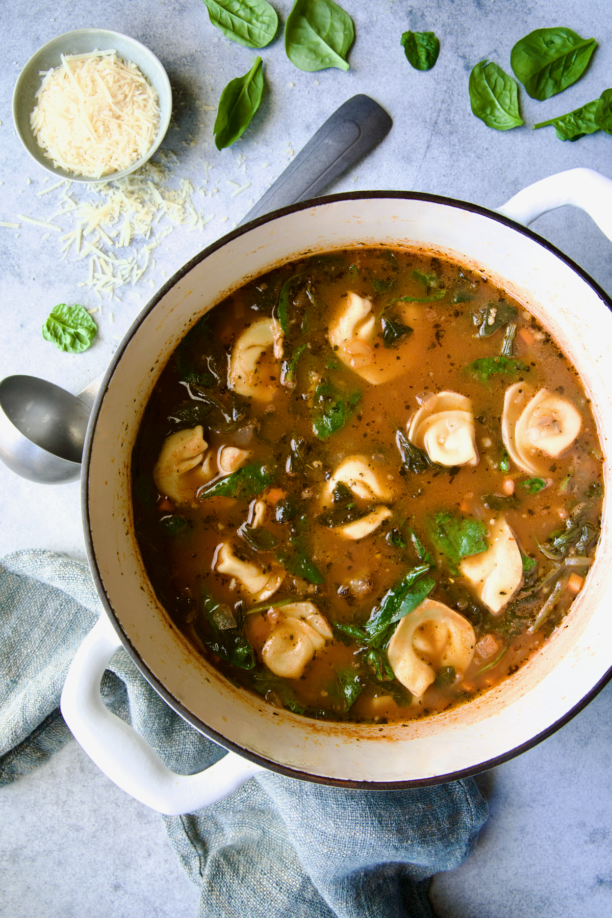 Finished Sausage Spinach Tortellini Soup in white Dutch oven with soup ladle on the side.