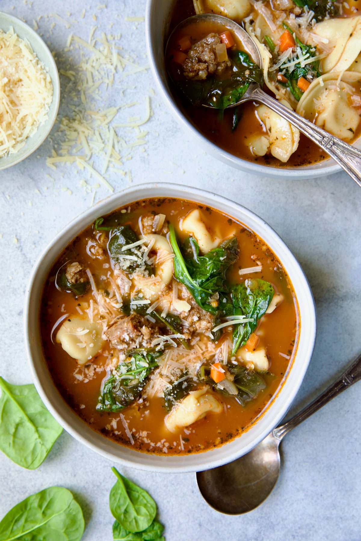 Two bowls of Sausage Spinach Tortellini Soup with ornate soup spoon sprinkled with grated Parmesan.