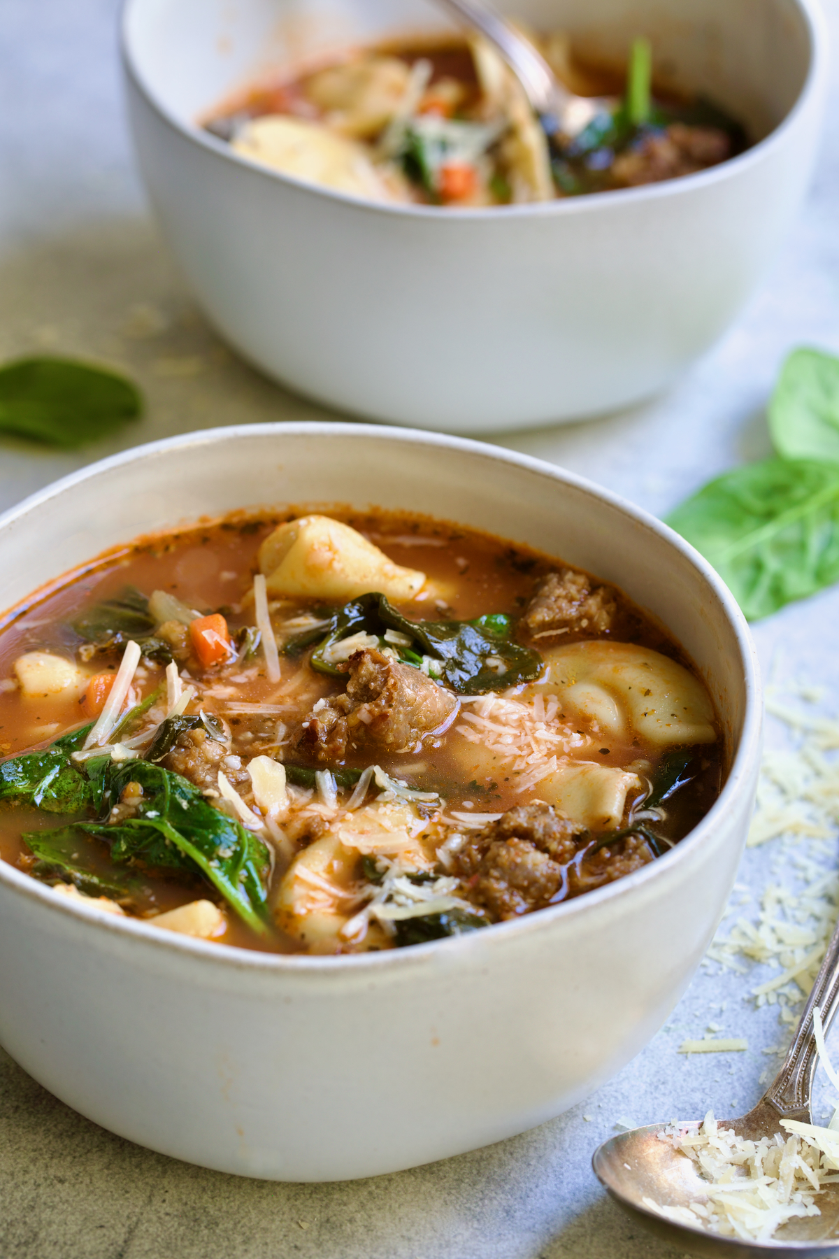Sausage Spinach Tortellini Soup in white bowl with ornate soup spoon sprinkled with grated Parmesan.