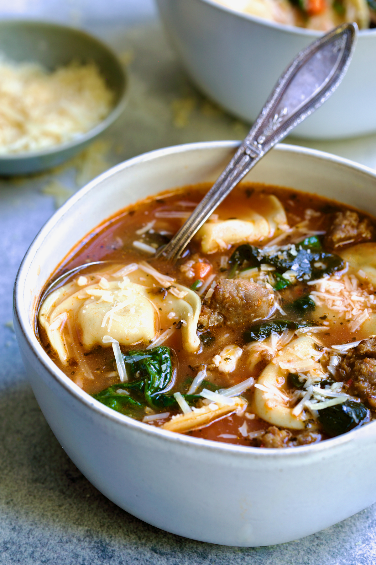 Sausage Spinach Tortellini Soup in white bowl with ornate soup spoon sprinkled with grated Parmesan.