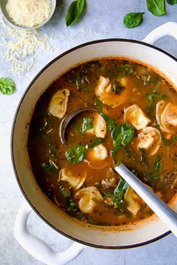 Sausage Spinach Tortellini Soup in white Dutch oven with soup ladle.