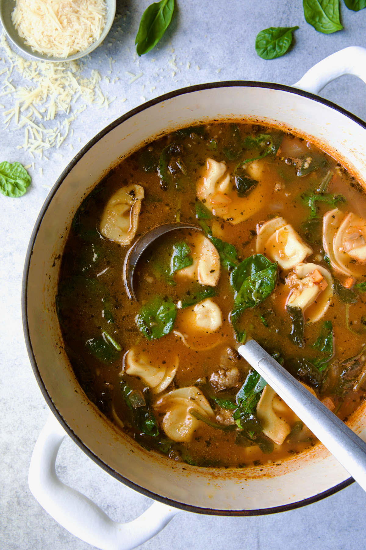 Sausage Spinach Tortellini Soup in white Dutch oven with soup ladle.