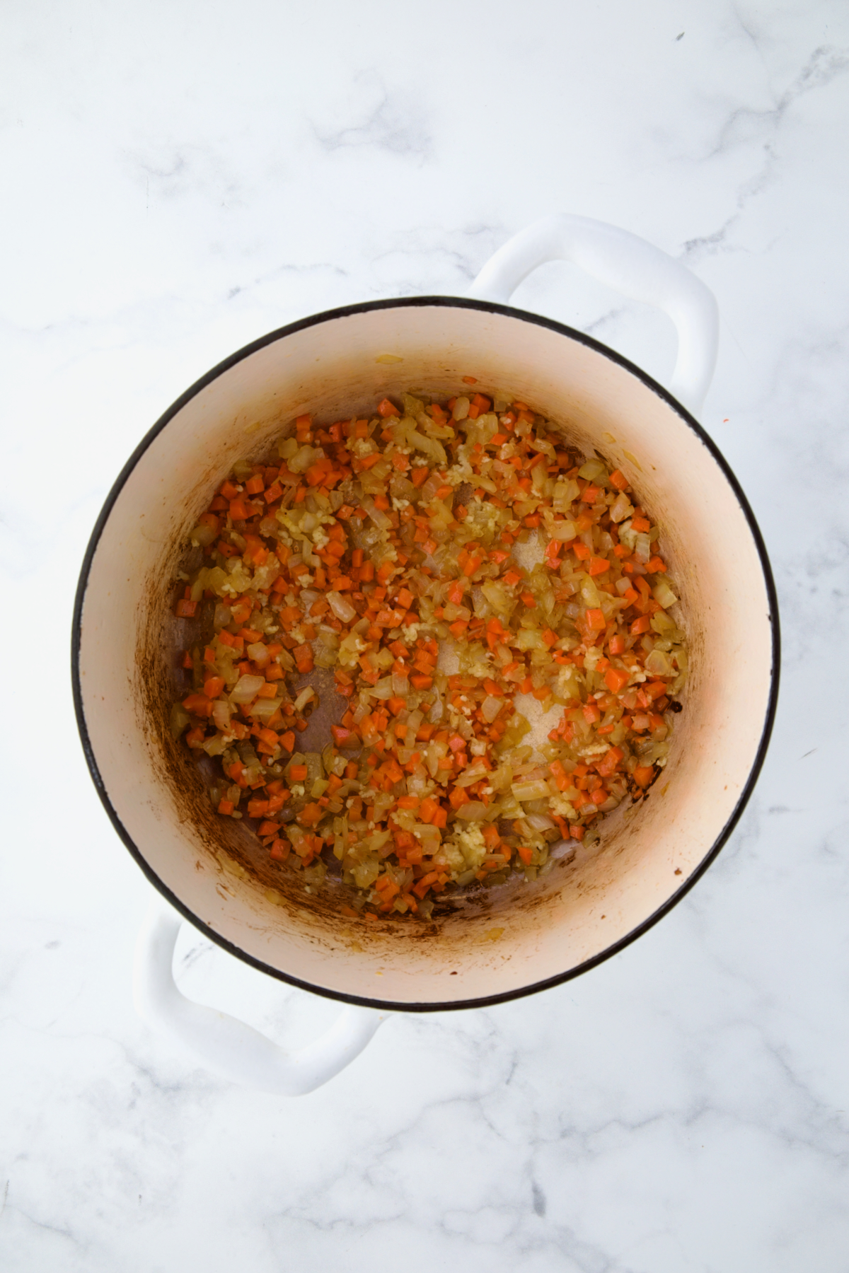 Cooked onion and carrot in white Dutch oven.