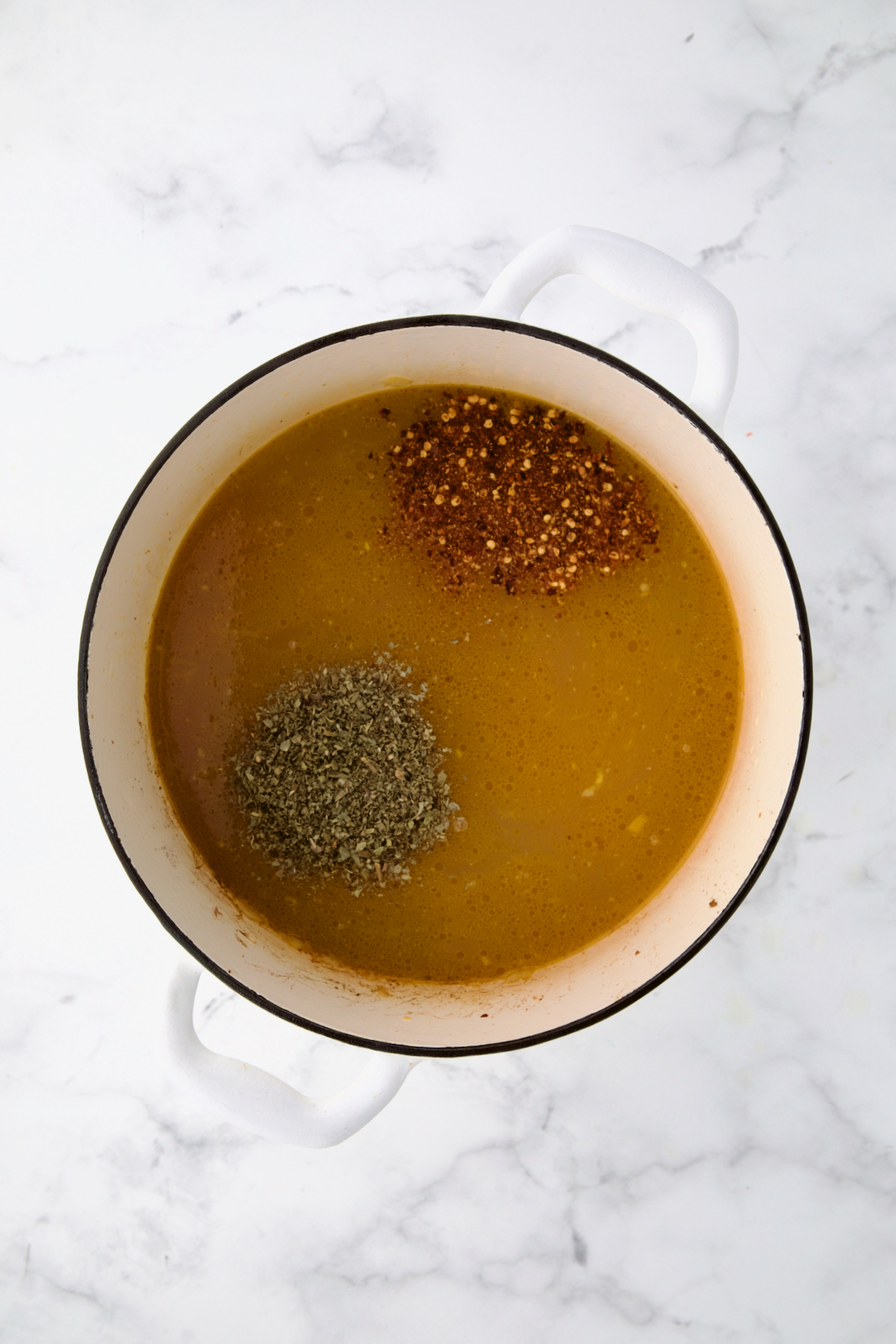 Italian seasoning and crushed red pepper flakes added to chicken broth in white Dutch oven.