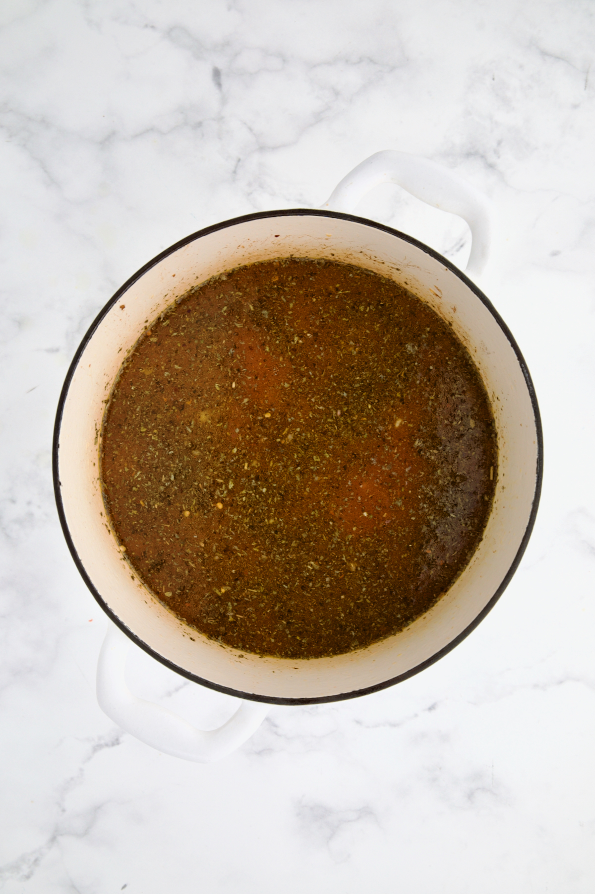 Tomato sauce added to chicken broth and herbs in white Dutch oven.