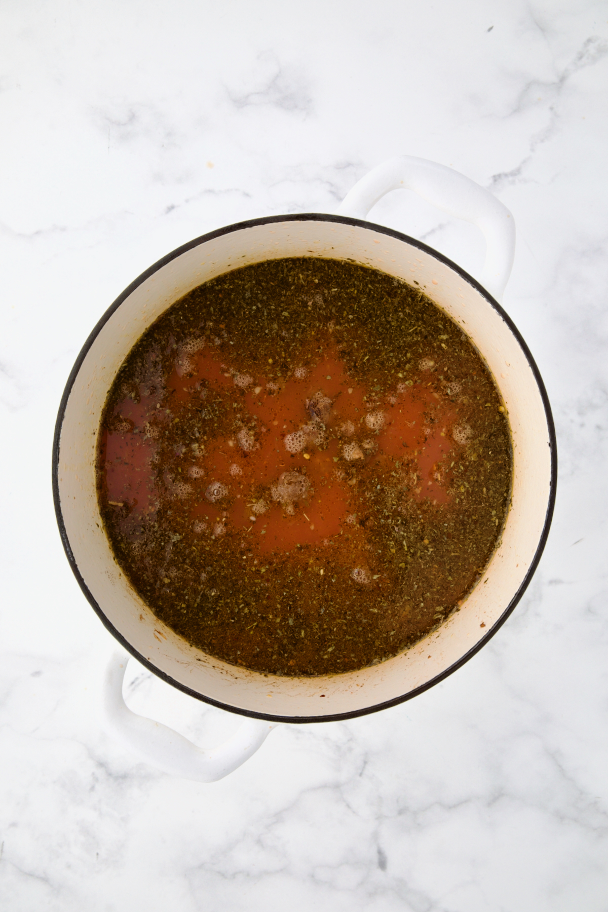 Tomato sauce added to chicken broth and herbs in white Dutch oven.