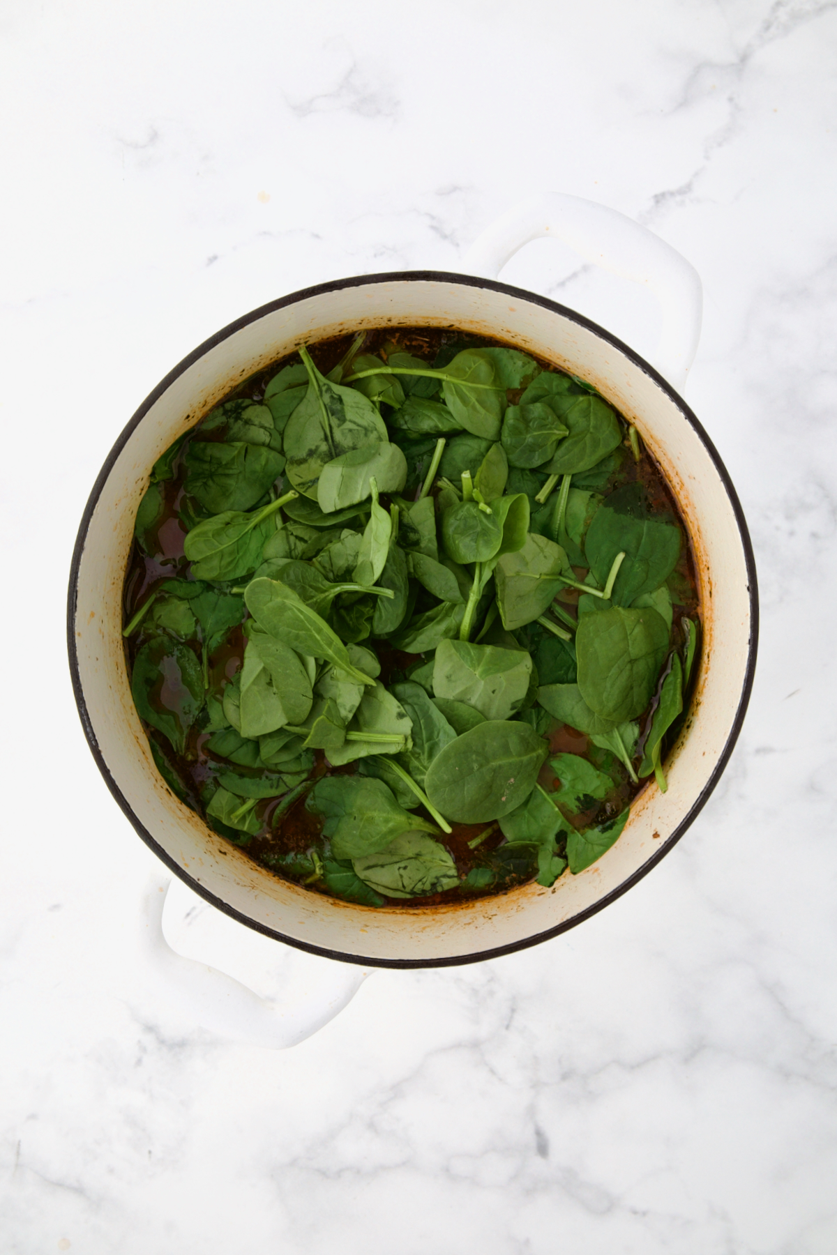 Spinach added to soup in white Dutch oven.