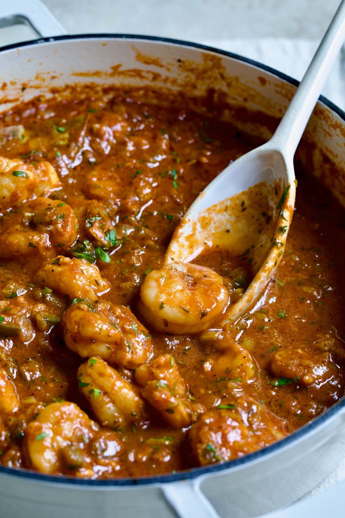Finished Best Shrimp Creole in white enamel cast iron skillet with serving spoon scooping up one of the shrimp.