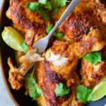 Thai Red Curry Chicken Legs on black platter garnished with cilantro and lime wedges with serving fork.