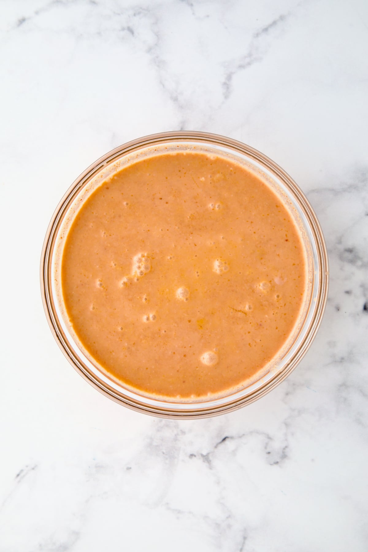 Coconut milk, red curry paste, garlic, ginger, and fish sauce combined in glass bowl.