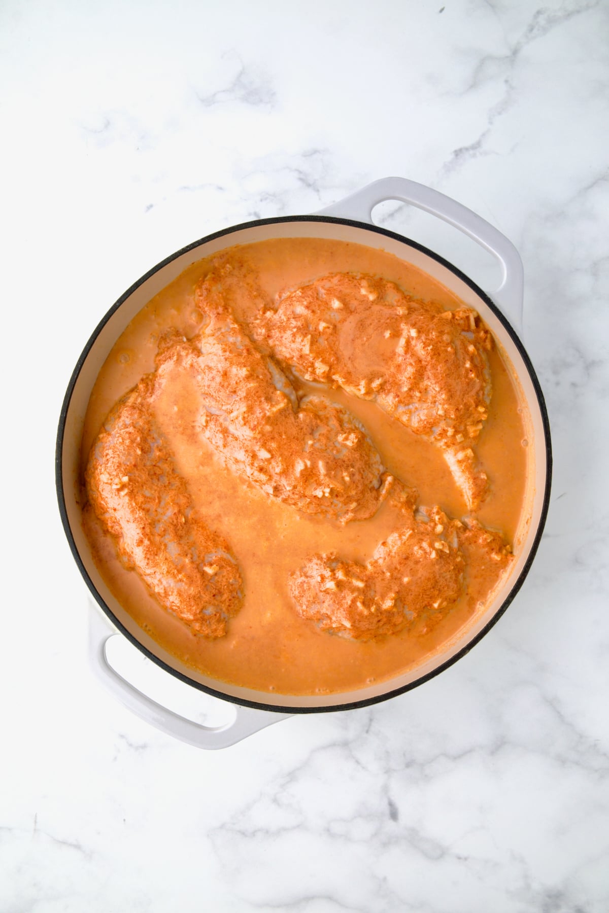 Coconut milk combination poured over chicken legs in white enamel cast iron skillet.