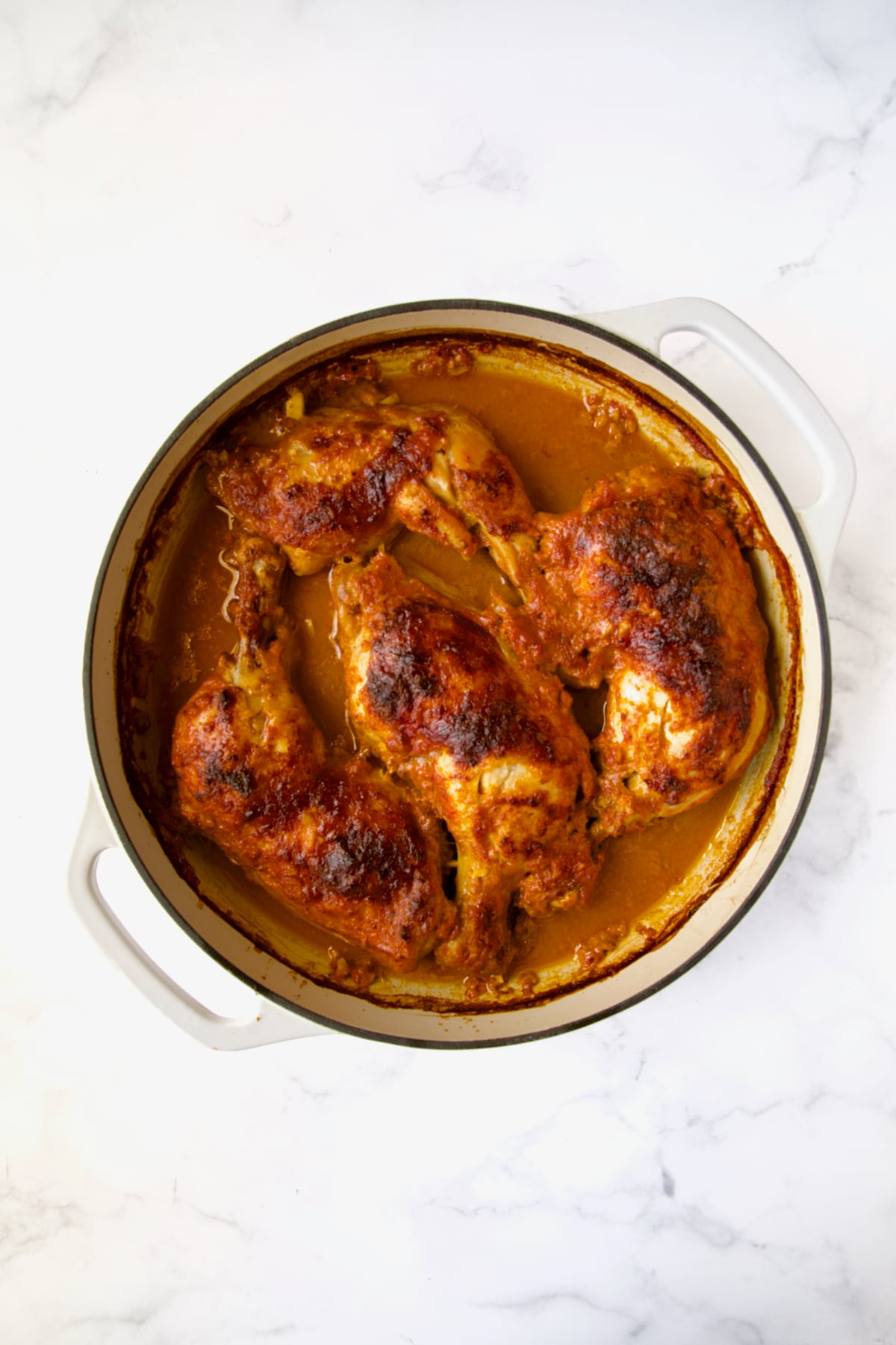 Braised chicken legs in white enamel cast iron skillet without any garnishes.