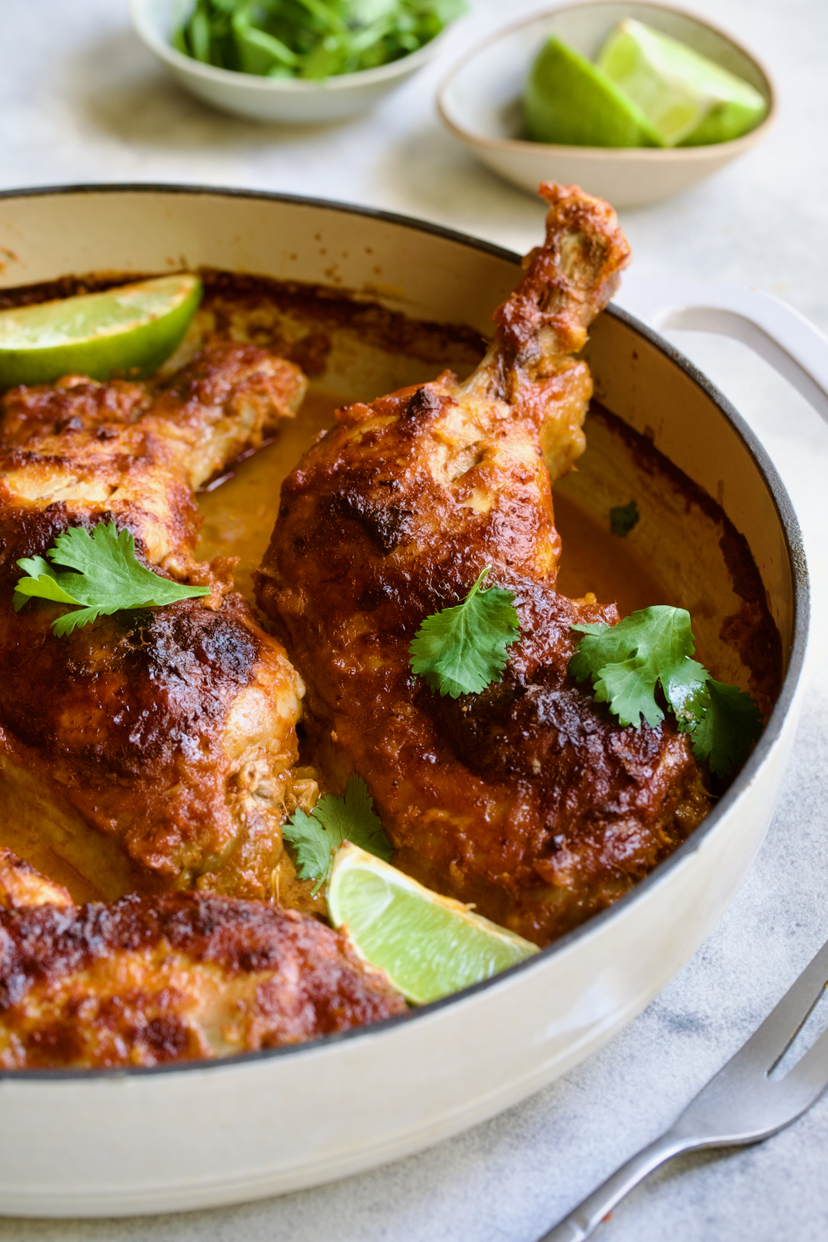 Thai Red Curry Braised Chicken Legs in white enamel cast iron skillet garnished with cilantro and lime wedges.