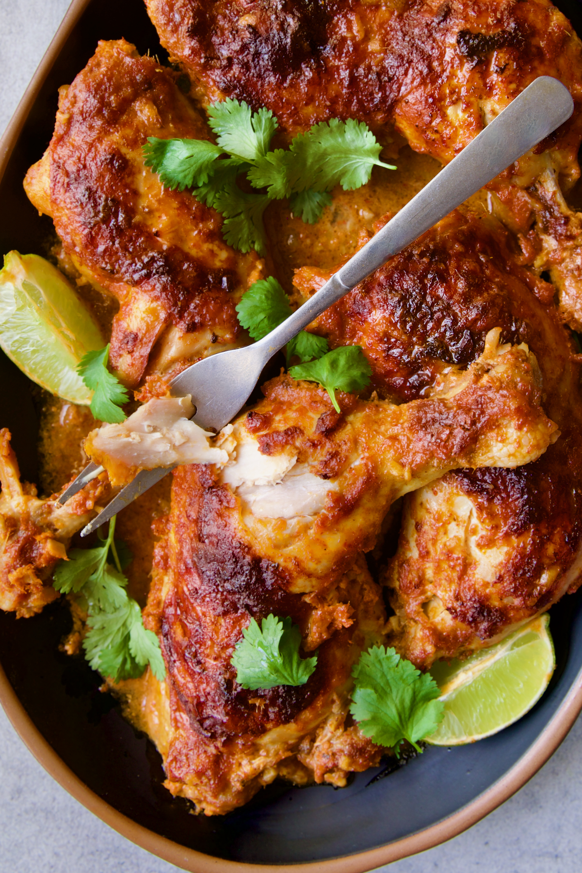 Thai Red Curry Braised Chicken Legs on black platter garnished with cilantro and lime wedges with serving fork.