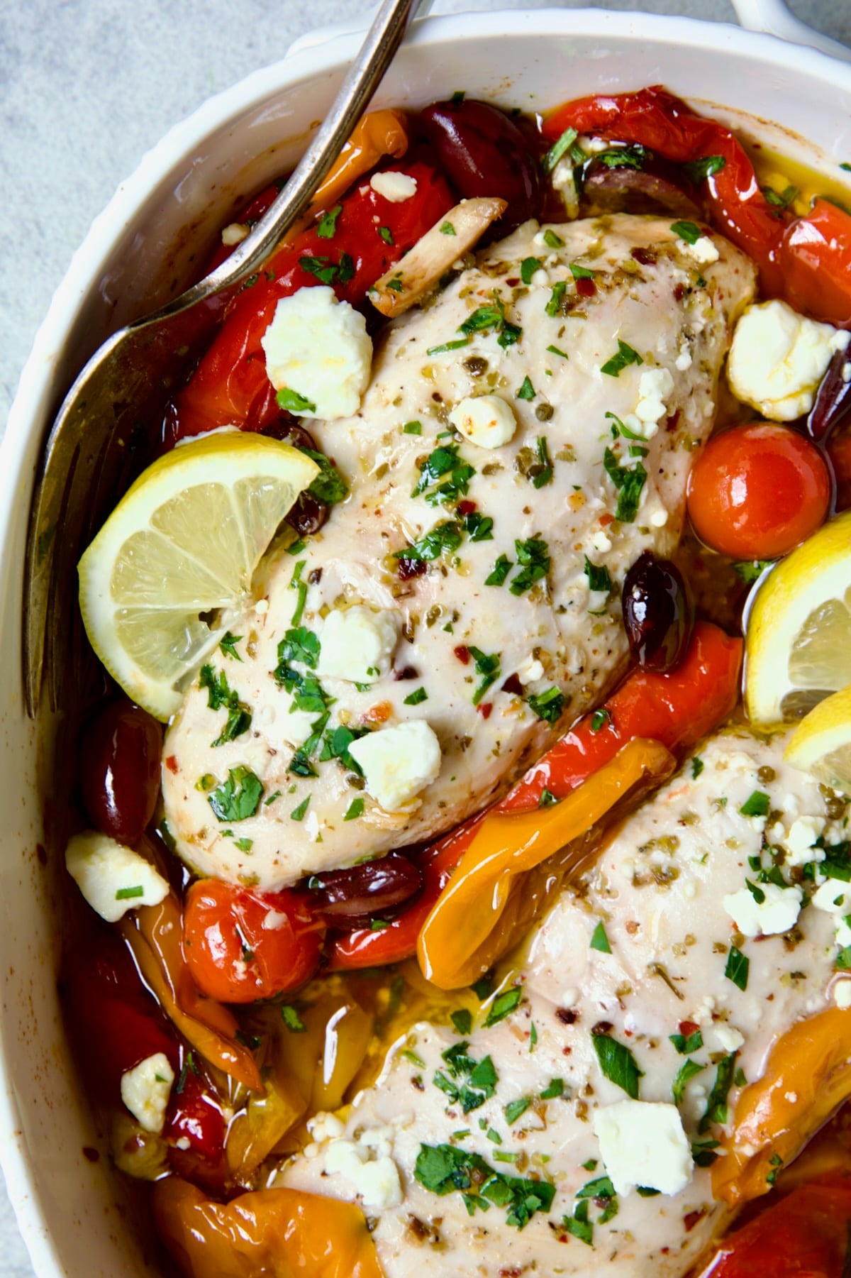 Greek Baked Chicken in white oval baking dish with serving fork.