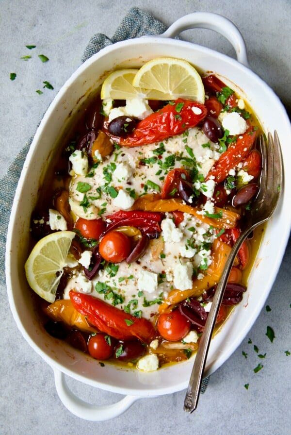 Greek Baked Chicken in white oval baking dish with serving fork.