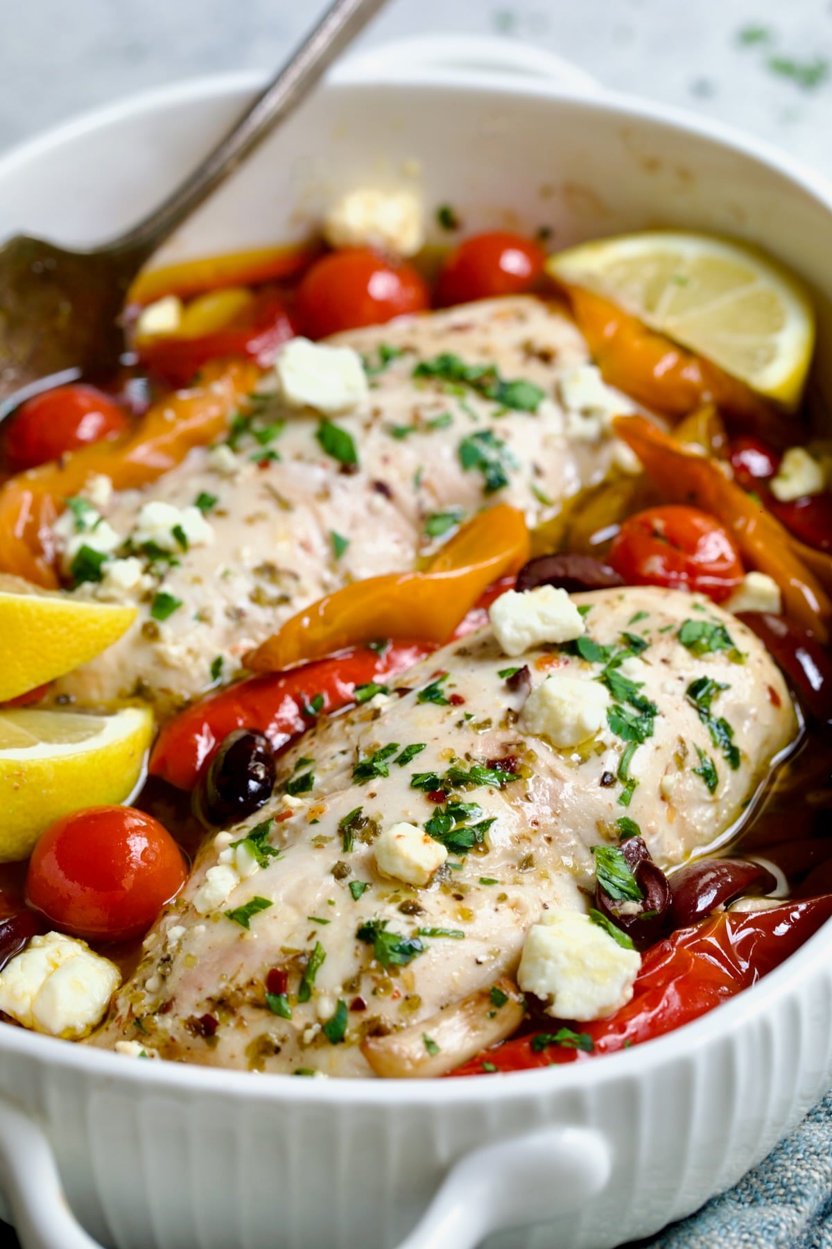 Greek Baked Chicken in white oval baking dish with serving fork.