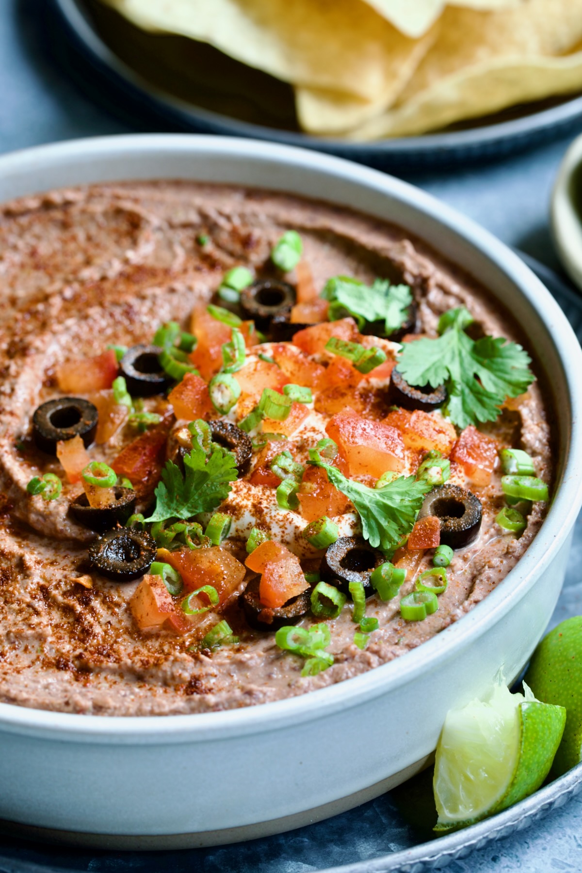 Black Bean Dip in white clay bowl with tortilla chips and lime wedges.
