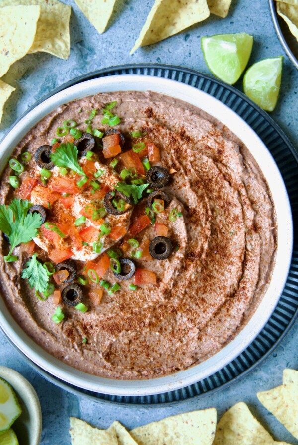 Black Bean Dip in white clay bowl with tortilla chips and lime wedges scattered about.