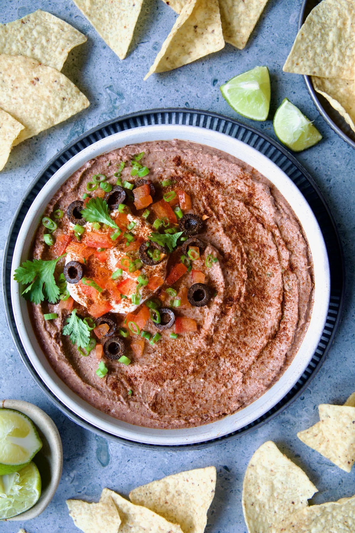 Black Bean Dip in white clay bowl with tortilla chips and lime wedges scattered about.
