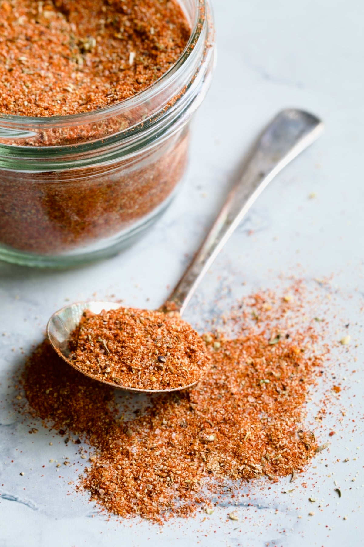 Spoon of Blackening Seasoning spilling over onto surface with jar in the background.