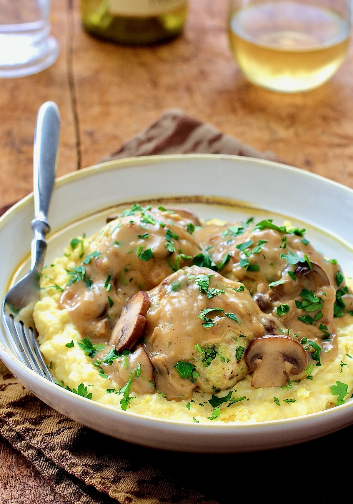 Chicken Meatballs Marsala with Parmesan Polenta in white bowl with fork.
