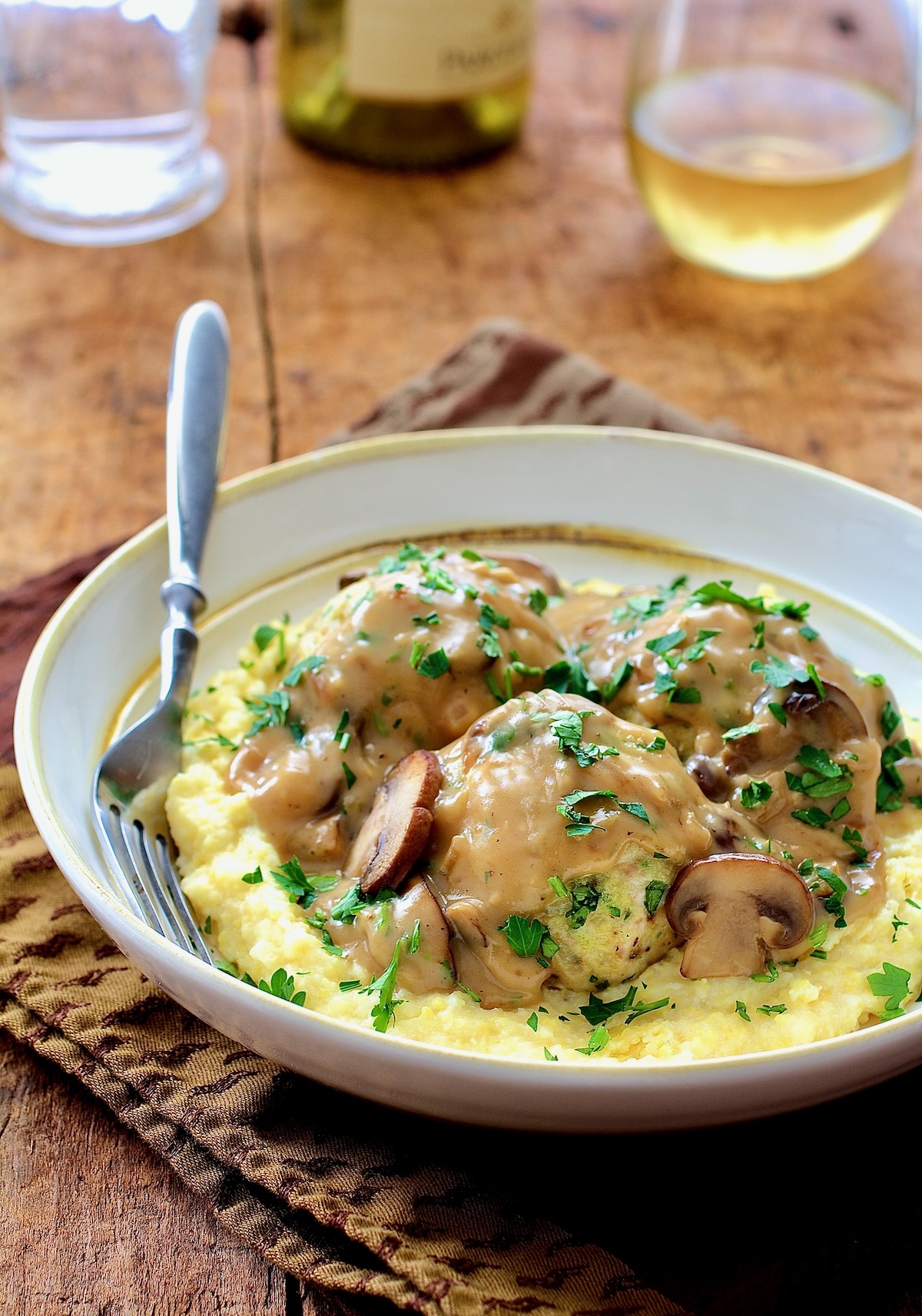 Chicken Meatballs Marsala with Parmesan Polenta in white bowl with fork.