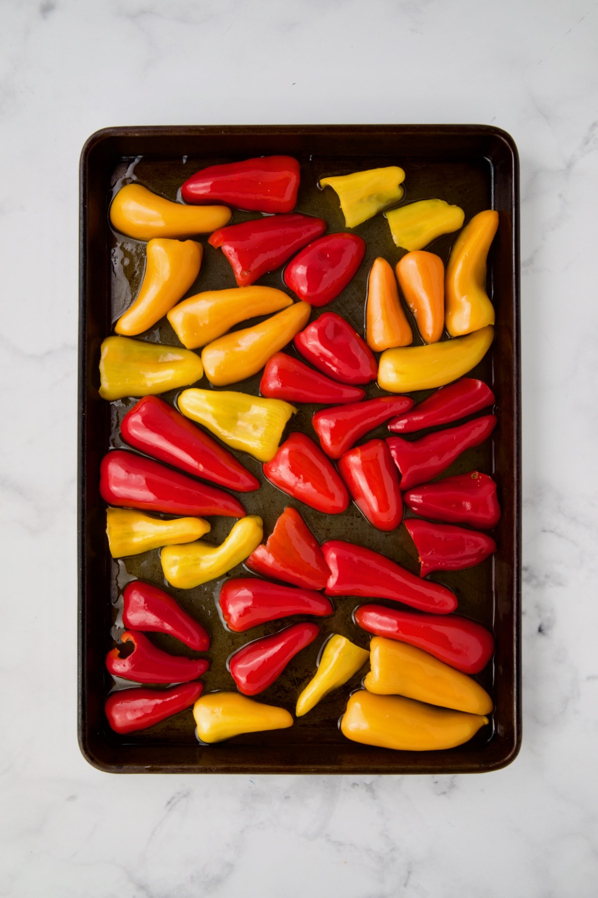 Halved mini peppers before being roasted on rimmed sheet pan drizzled with olive oil.