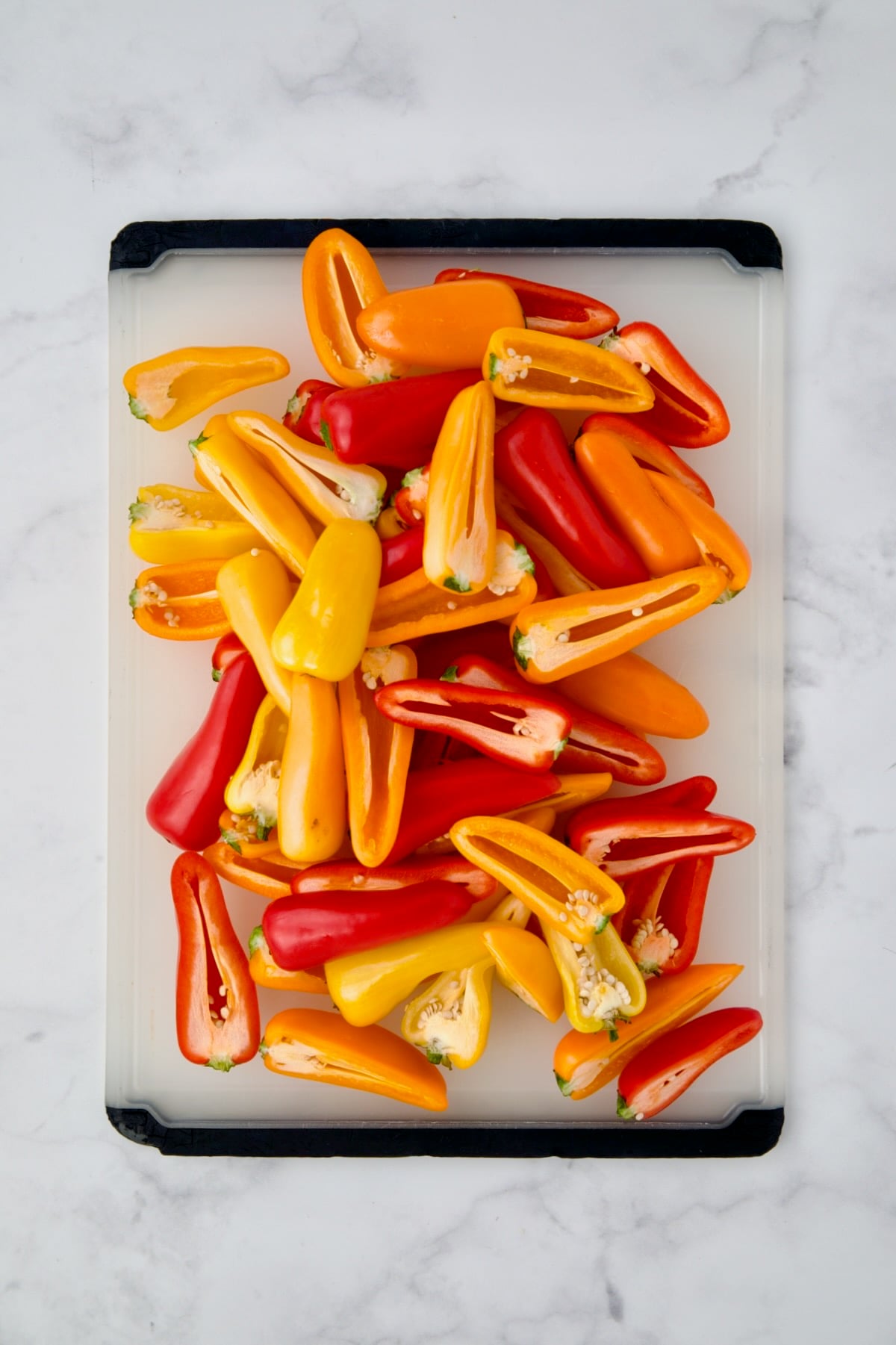Pile of halved yellow and red on white plastic cutting board before seeds and membranes are removed.