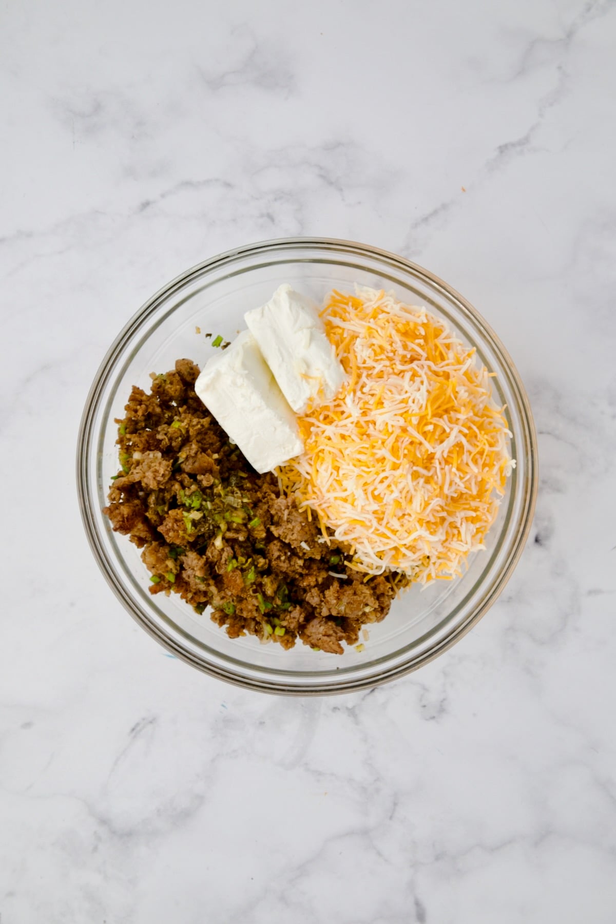 Cooked sausage, cream cheese and Mexican blend shredded cheese in glass bowl before being combined.
