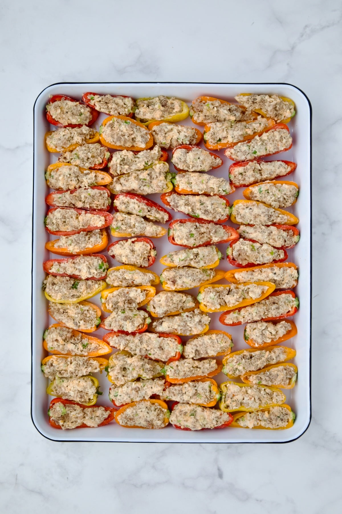 Stuffed mini peppers on white enamel rimmed baking sheet before being baked.