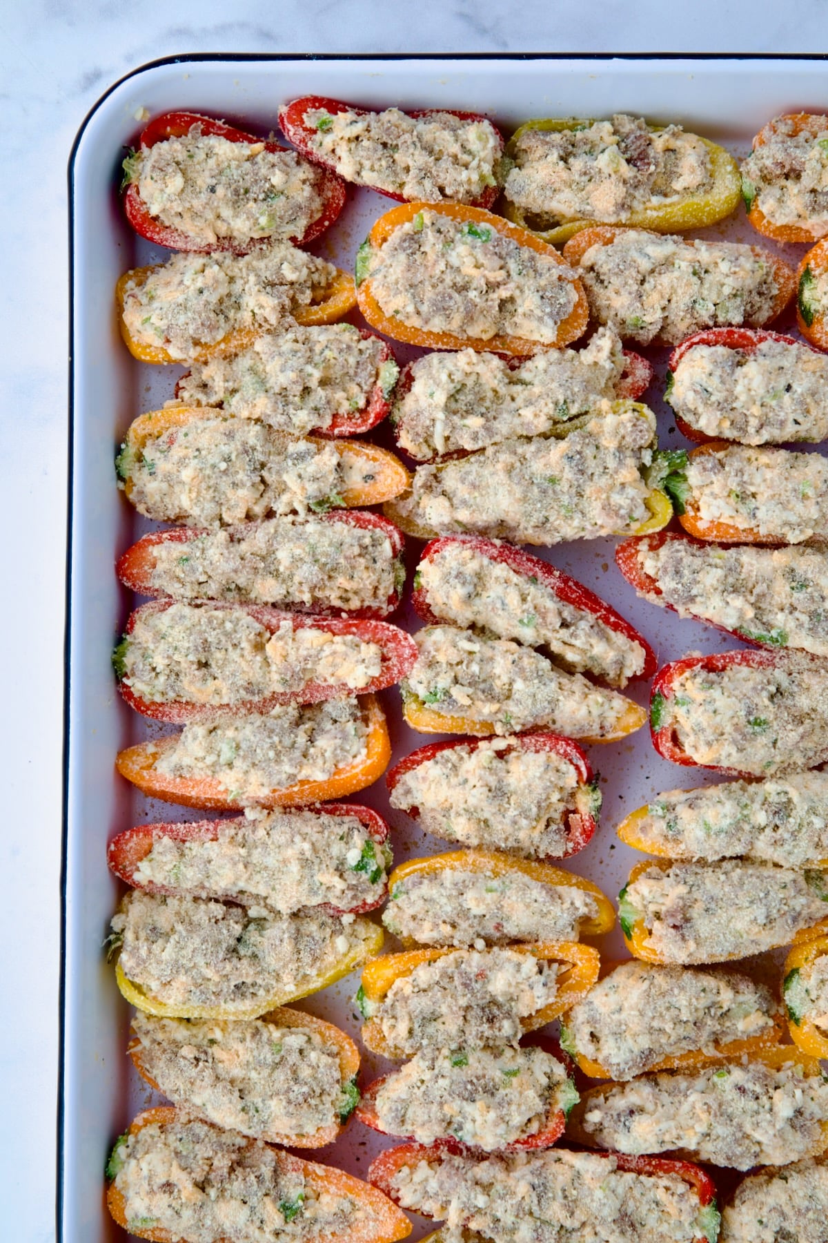 Stuffed mini peppers on white enamel rimmed baking sheet with breadcrumbs sprinkled on.