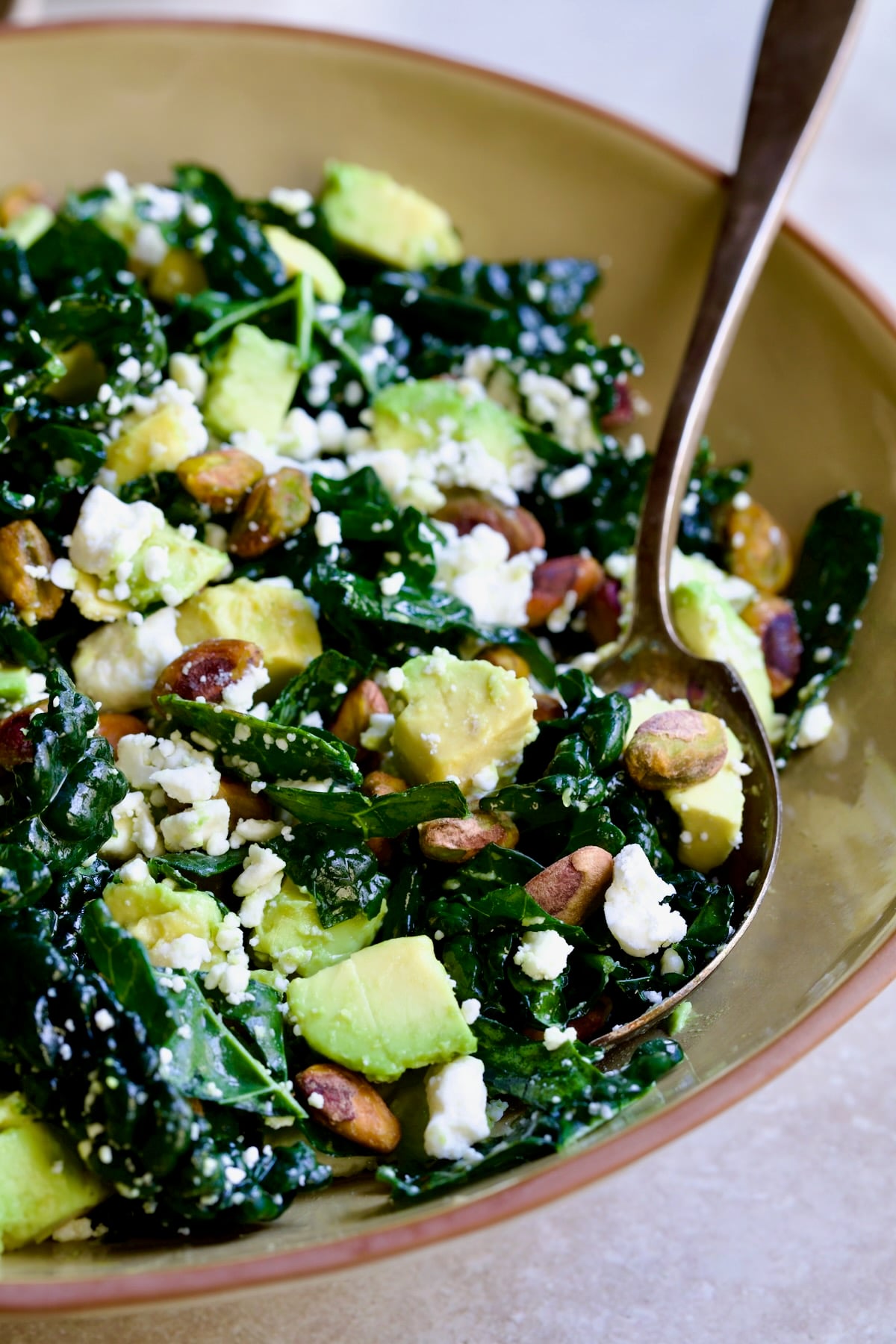 Tuscan Kale Salad with Lemon Tahini Dressing in beige bowl with serving spoon scooping some up.